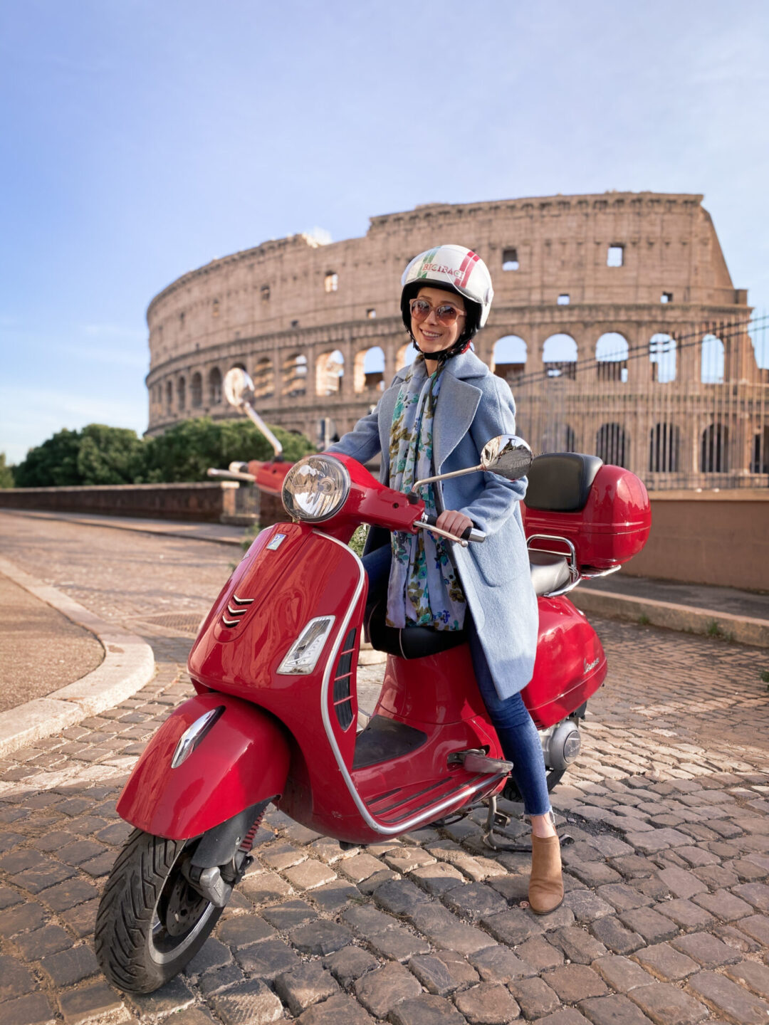 Travel Blogger Jordan Gassner smiling while riding a red vespa on a road just alongside the Colosseum in Rome, Italy