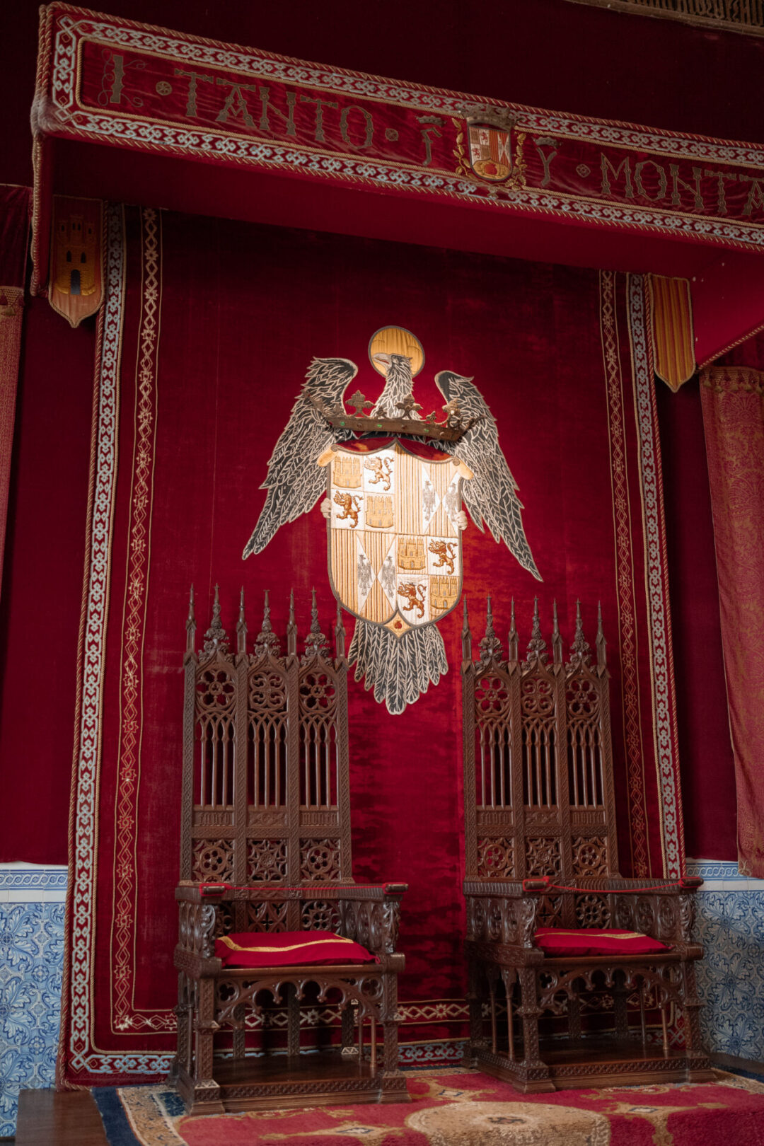 The wooden thrones in front of a red tapestry-decorated wall inside the Alcazar in Segovia, Spain