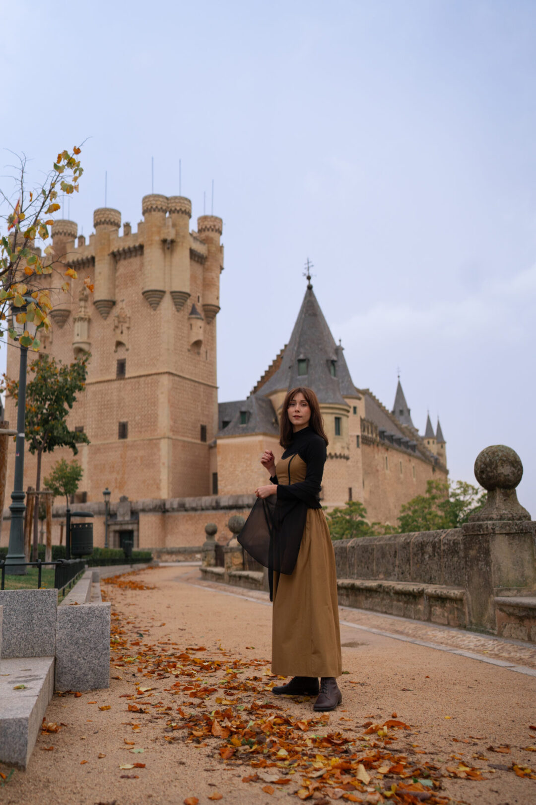 Travel Blogger Jordan Gassner wearing a long dress and looking toward camera in front of the Segovia Alcazar in Central Spain