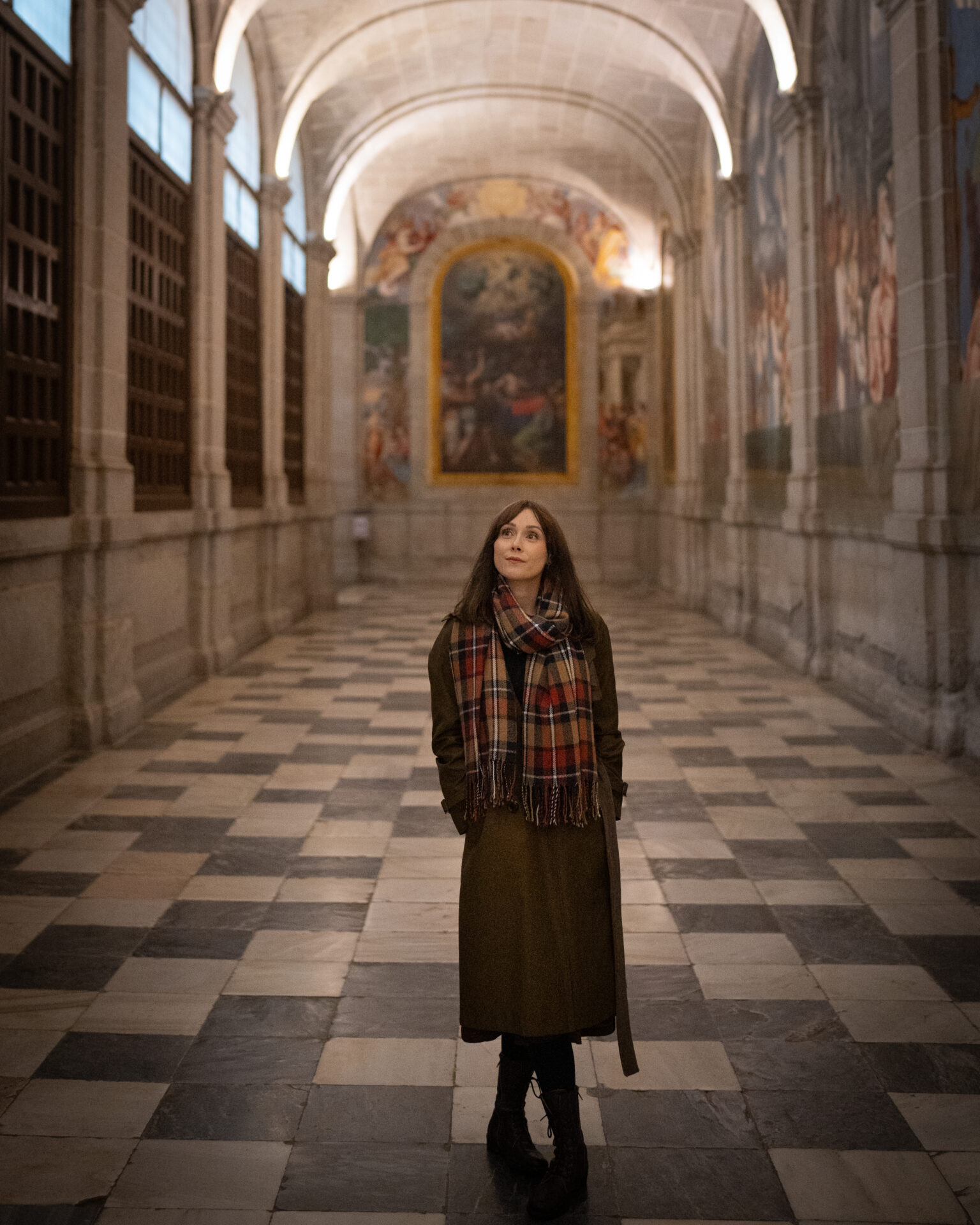 Travel Blogger Jordan Gassner standing inside an empty hallway decorated with large murals inside El Escorial in Spain