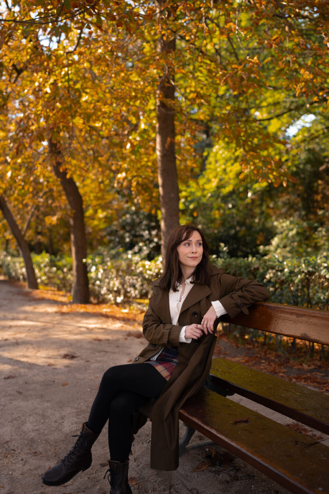 Travel Blogger Jordan Gassner looking over her shoulder to admire the fall foliage while sitting on a bench in Retiro Park in Madrid, Spain