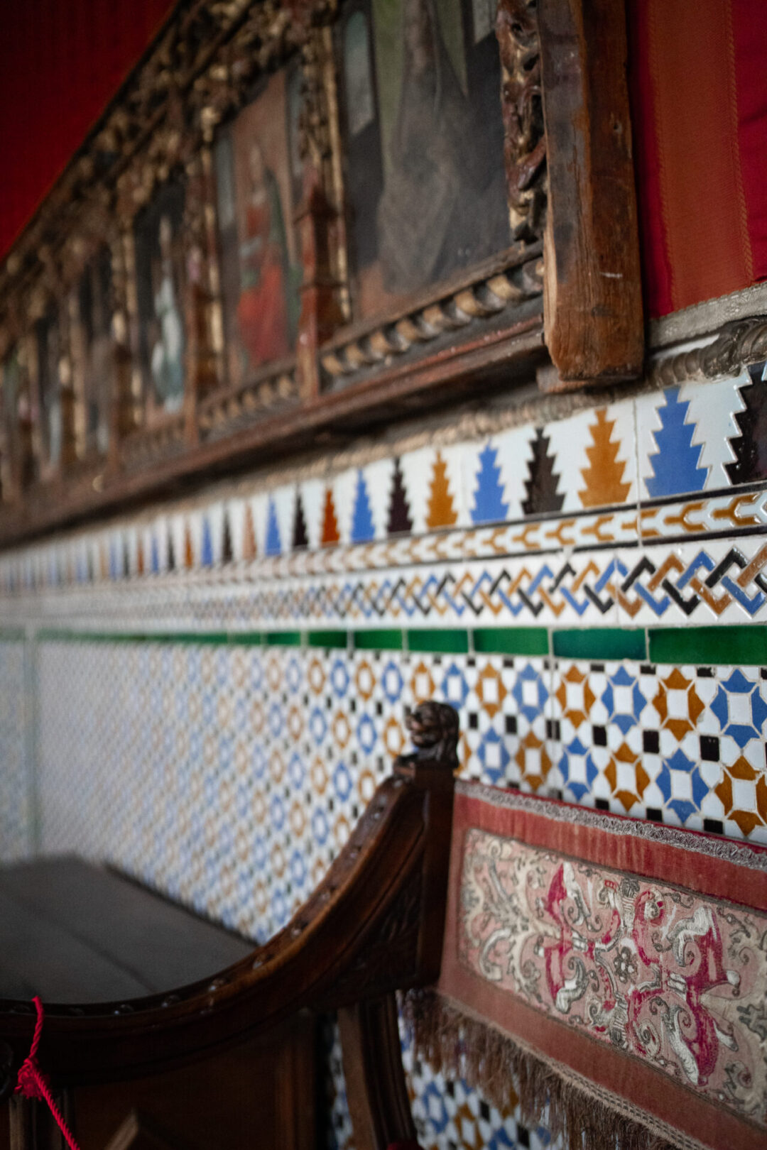 A medieval chair against a red wall decorated with blue, tan and brown tiles inside the Alcazar in Segovia, Spain