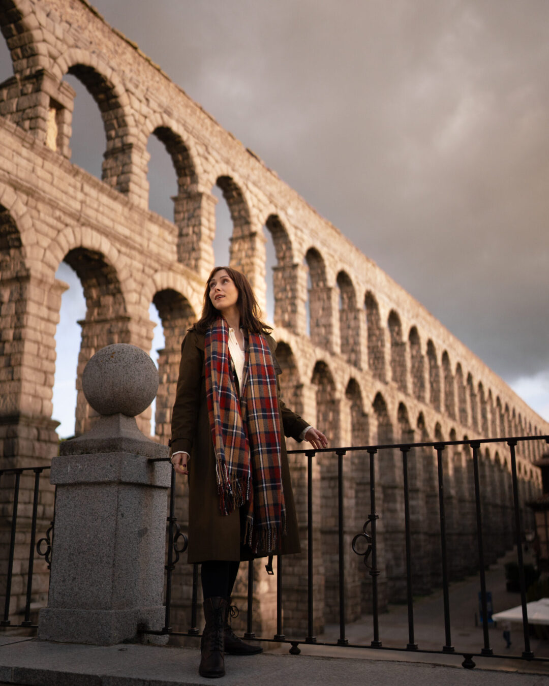 Travel Blogger Jordan Gassner turning around to look behind her at a tall Roman aqueduct from a lookout point in Segovia, Spain