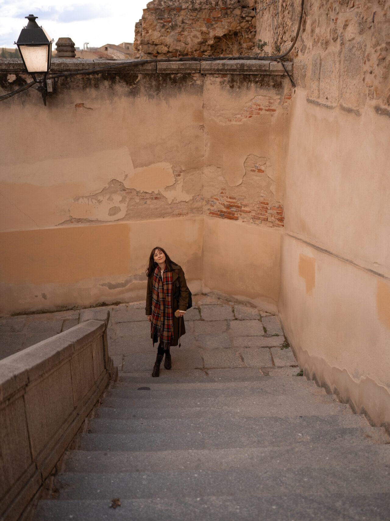 Travel Blogger Jordan Gassner smiling from the bottom of a set of stairs next to the Segovia Aqueduct in Central Spain
