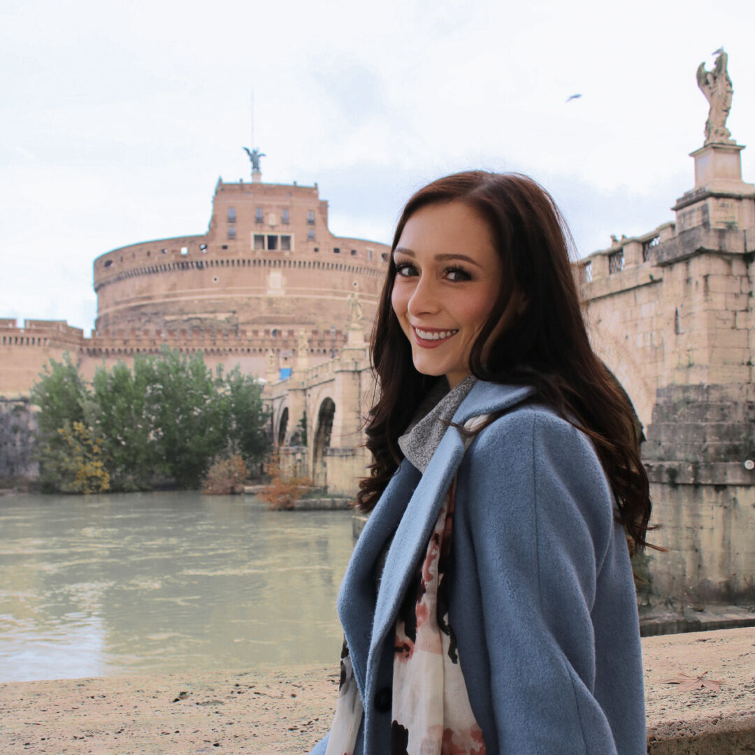 Roman Holiday Travel Guide: Travel Blogger Jordan Gassner smiling across the Tiber river from Castel Sant Angelo in Rome, Italy