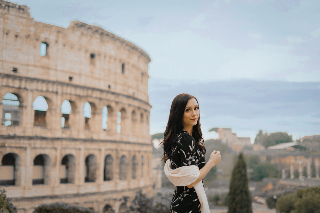Travel Blogger Jordan Gassner looking over her shoulder in front of the Colosseum in Rome, Italy