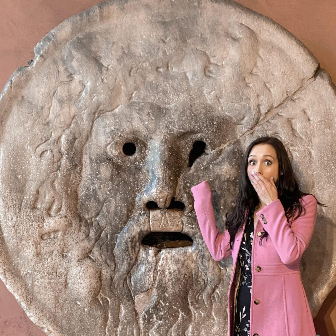 Travel Blogger Jordan Gassner mocking a "shocked" expression while hiding her hand in her jacket at the Mouth of Truth in Rome, Italy