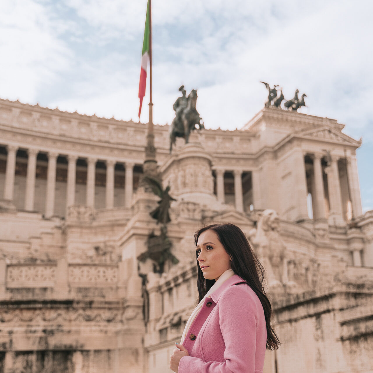 Travel Blogger Jordan Gassner wearing a pink coat outside Piazza Venezia in Rome, Italy