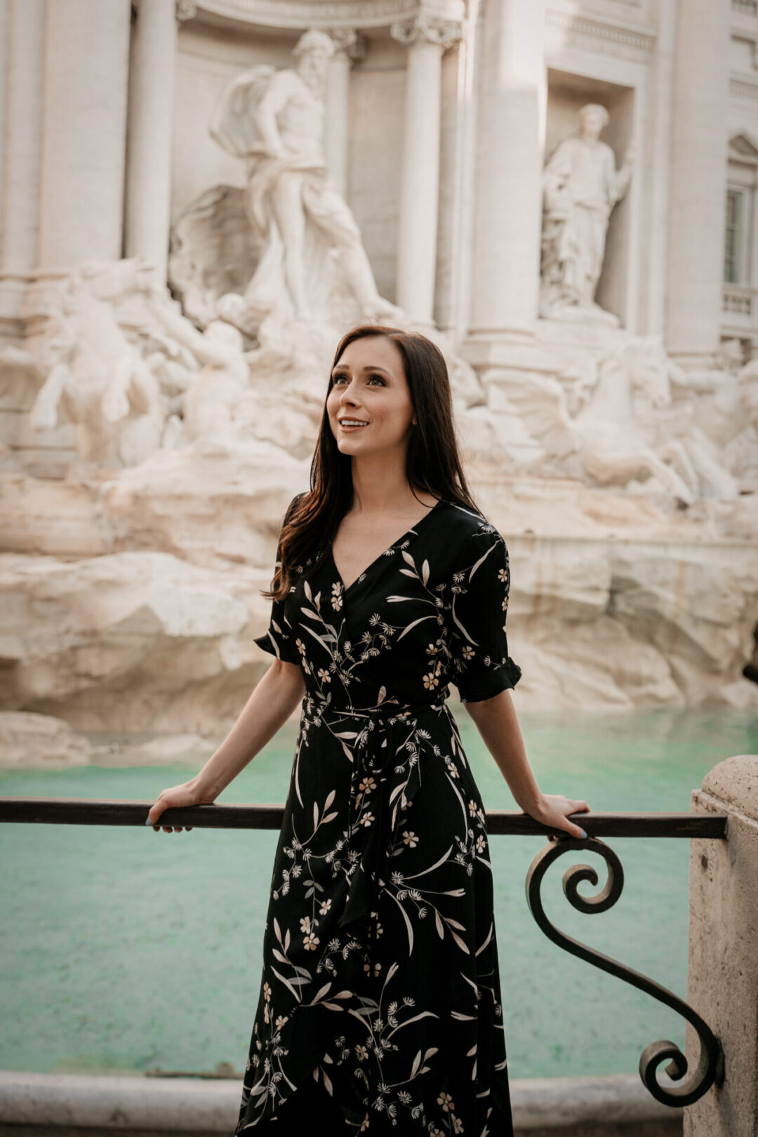 Roman Holiday Travel Guide: Travel Blogger Jordan Gassner smiling while standing against the railing of the Trevi Fountain in Rome, Italy