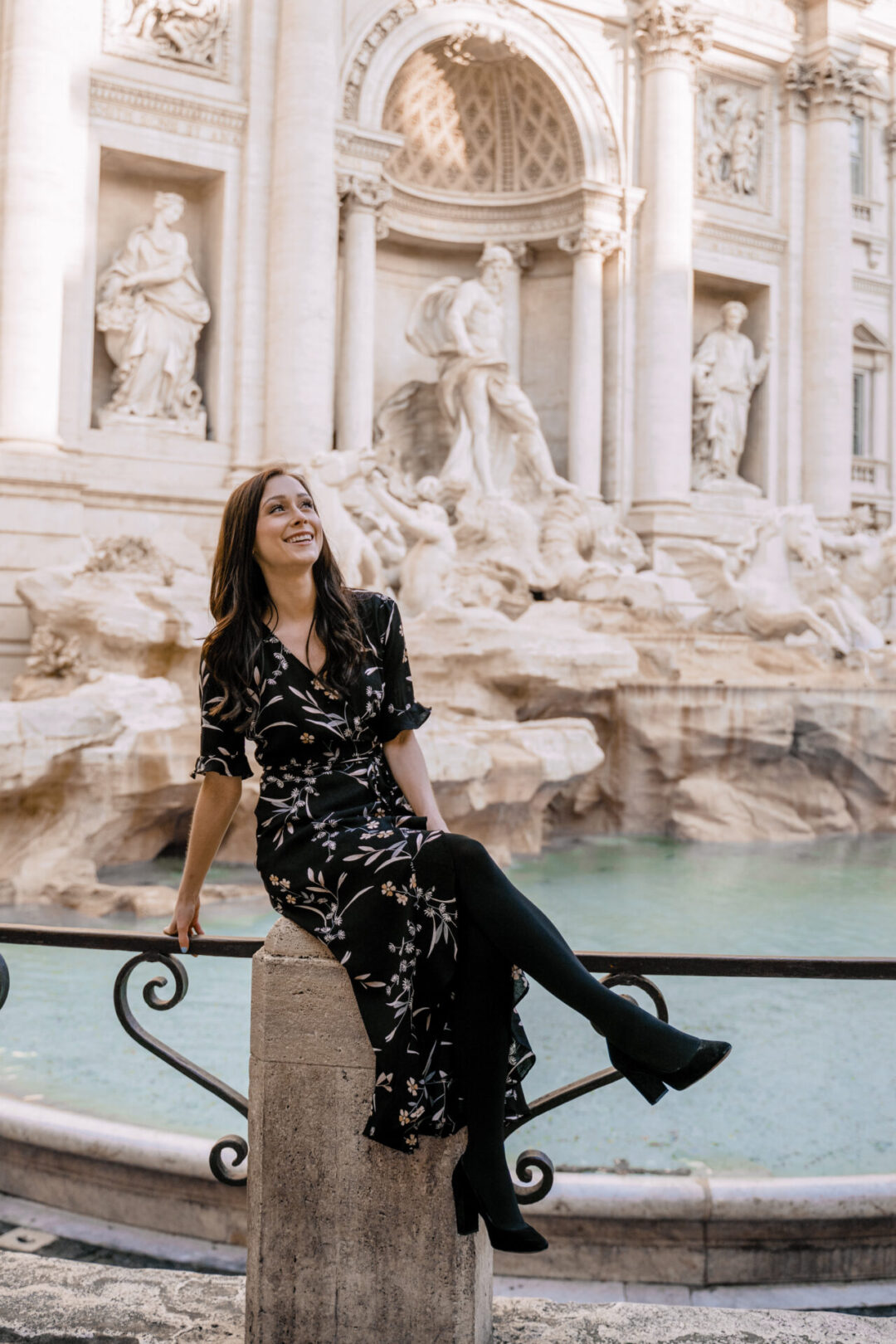 Travel Blogger Jordan Gassner sitting on a railing in front of the Trevi Fountain in Rome, Italy