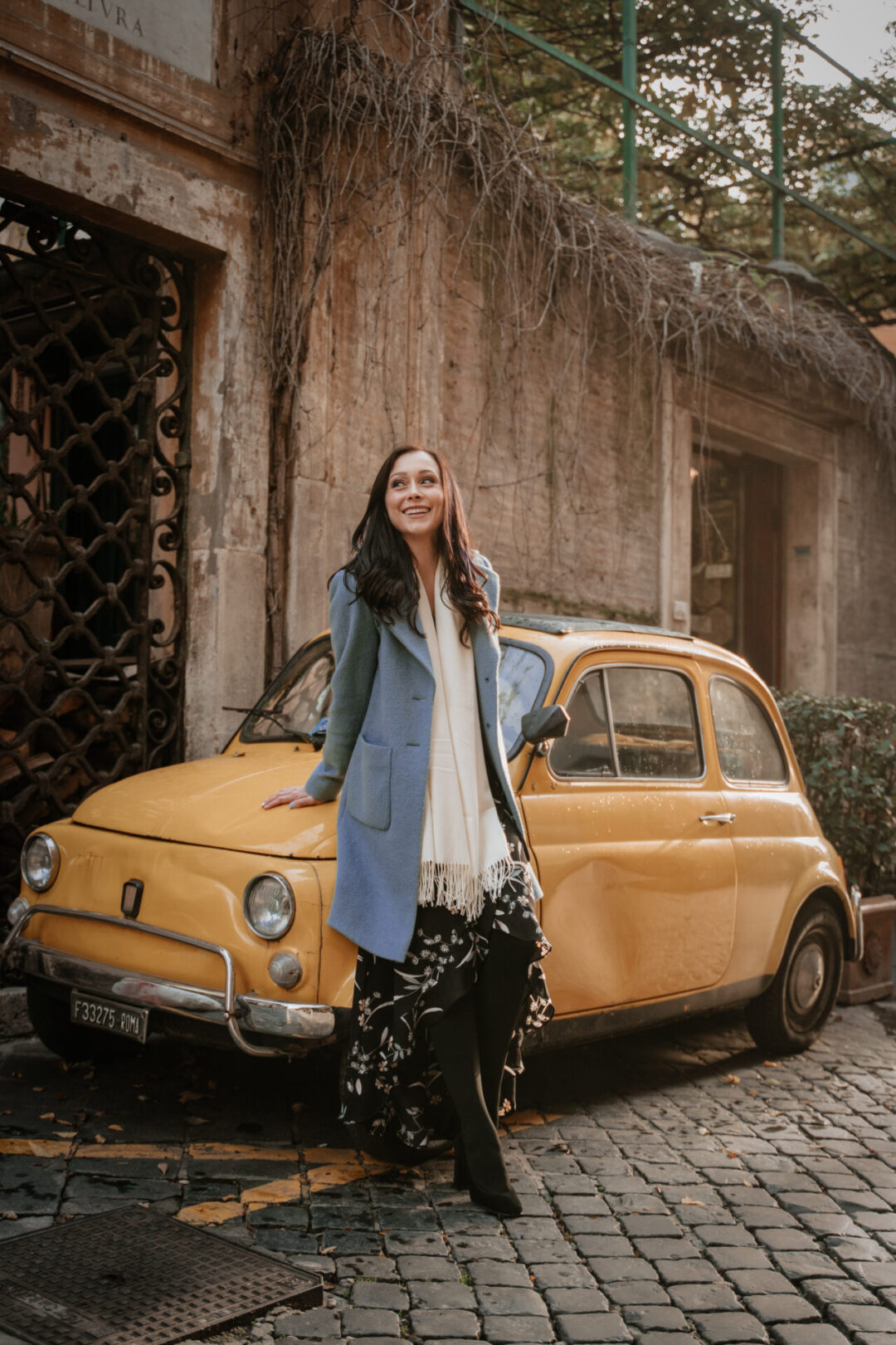 Travel Blogger Jordan Gassner smiling while leaning against a vintage yellow beetle on Via Margutta in Rome, Italy