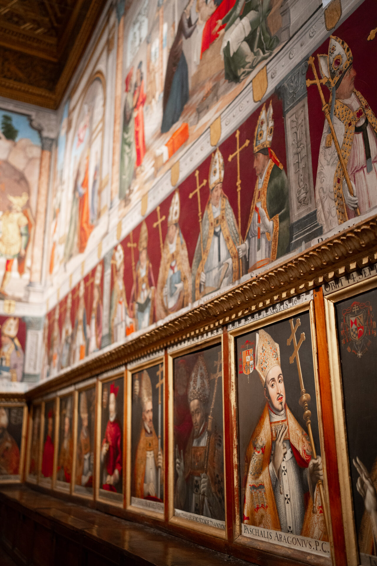 A wall of red with paintings of former bishops and cardinals in the Toledo Cathedral in Spain