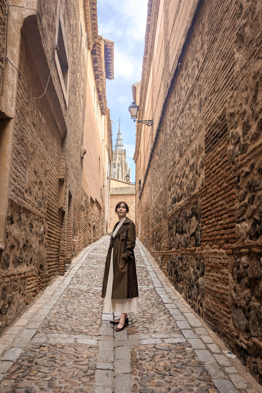 Travel Blogger Jordan Gassner standing in a small cobblestone alley with a view of the Toledo Cathedral in the background in the Old Town of Toledo, Spain near Madrid