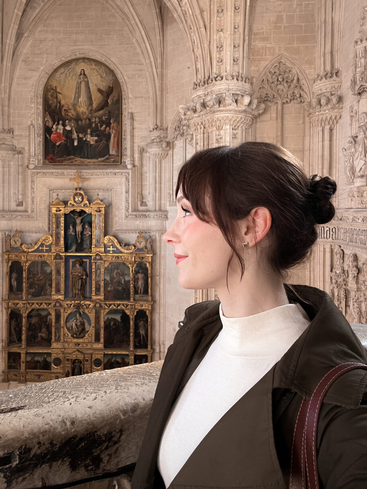 Travel Blogger Jordan Gassner smiling while looking out from a balcony with the altar in the background behind her inside the Monastery of San Juan de los Reyes in Toledo, Spain