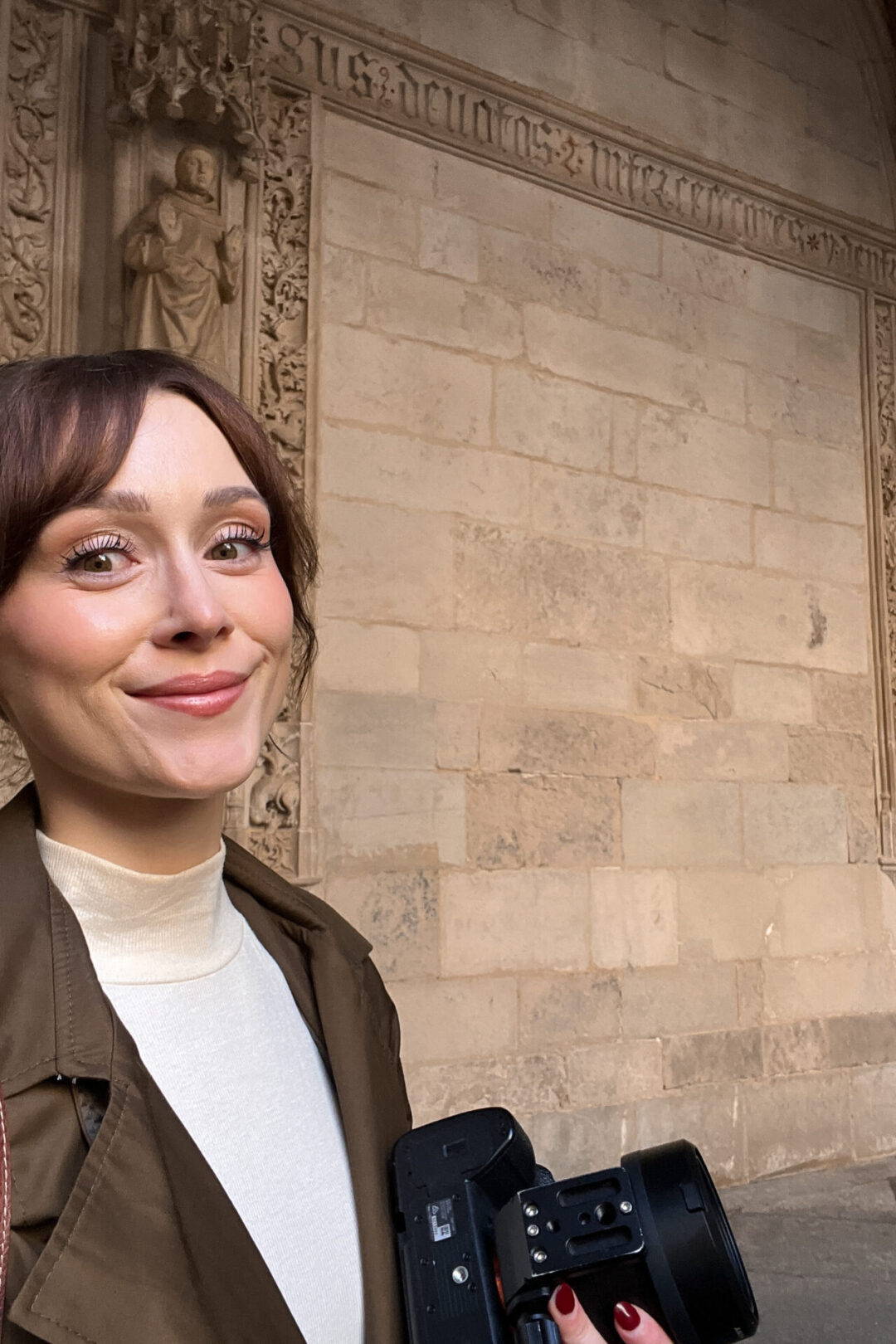 Travel Blogger Jordan Gassner smiling while holding her camera during a solo visit to a convent in Toledo Spain