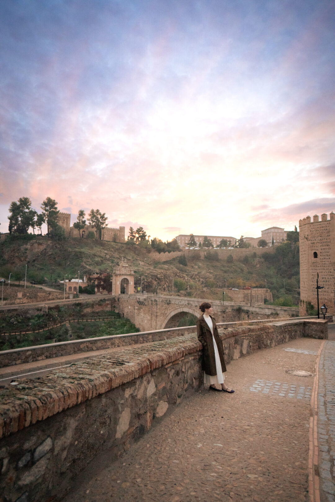 Travel Blogger Jordan Gassner standing on a sidewalk in front of the Alcantara Bridge at sunrise in Toledo, Spain