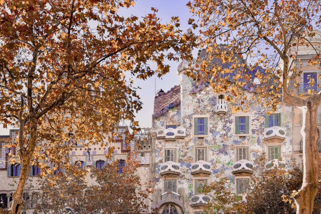 The UNESCO World Heritage site, Casa Batllo, from behind some red leafed trees in autumn in Barcelona, Spain