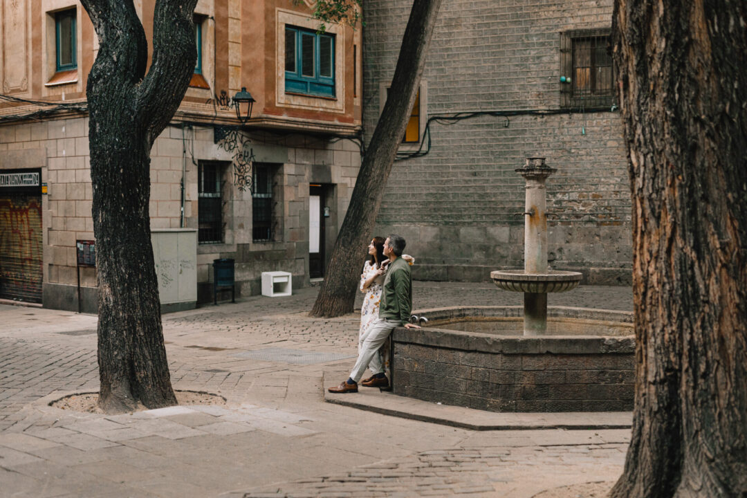 Travel Blogger Jordan Gassner and her partner leaning against a fountain and looking up at the buildings in the Gothic Quarter in Barcelona, Spain