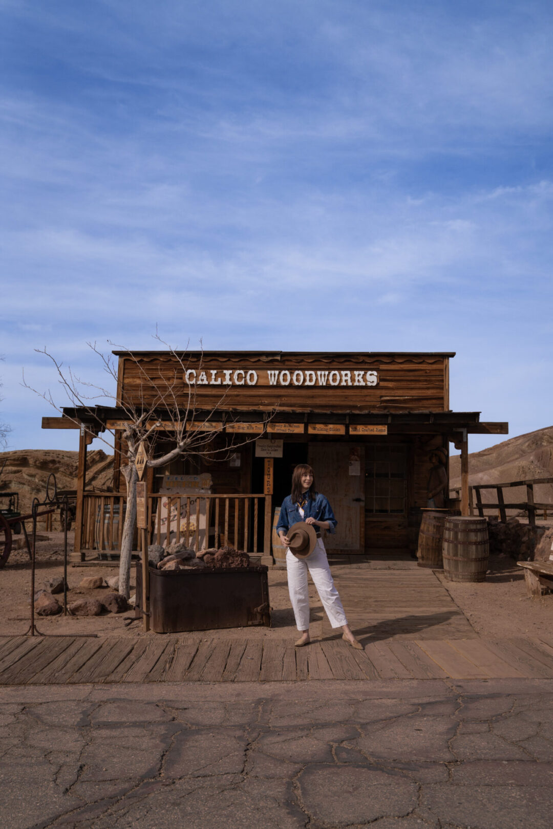 Travel Blogger Jordan Gassner holding her western hat in front of Calico Woodworks store at Calico Ghost Town in California