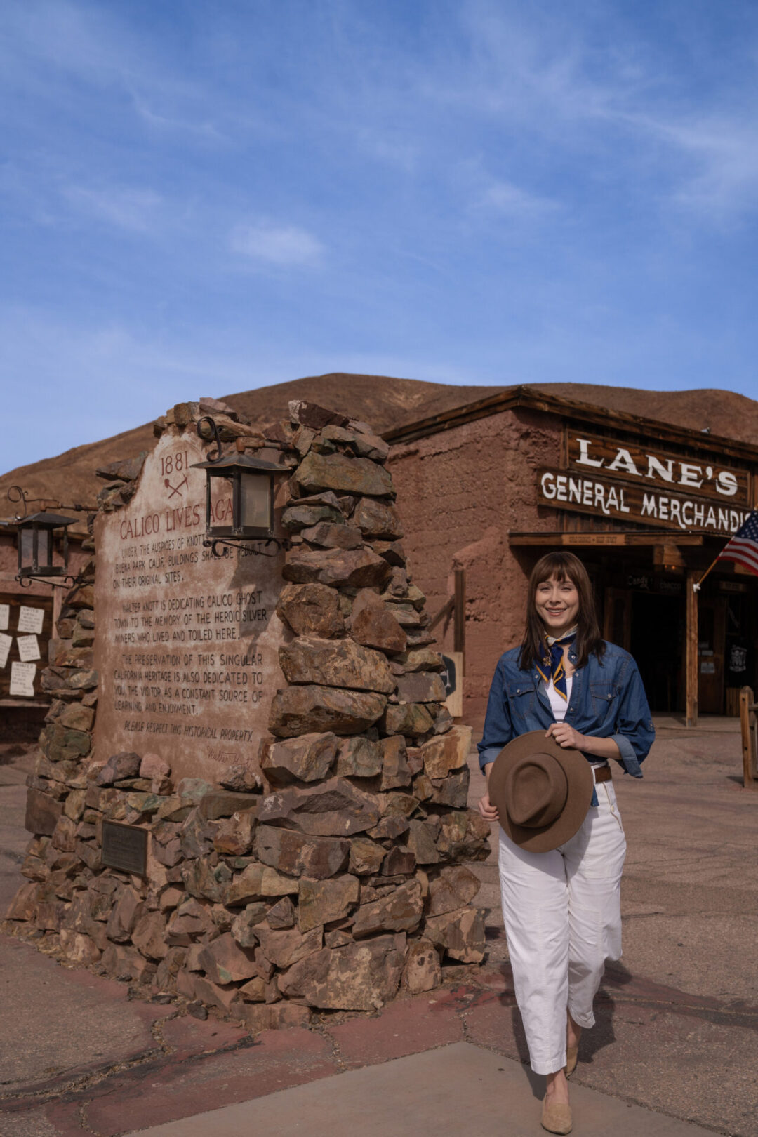 Travel Blogger Jordan Gassner holding her western hat while standing in front of the classic Lane's General Merchandise at Calico Ghost Town in California