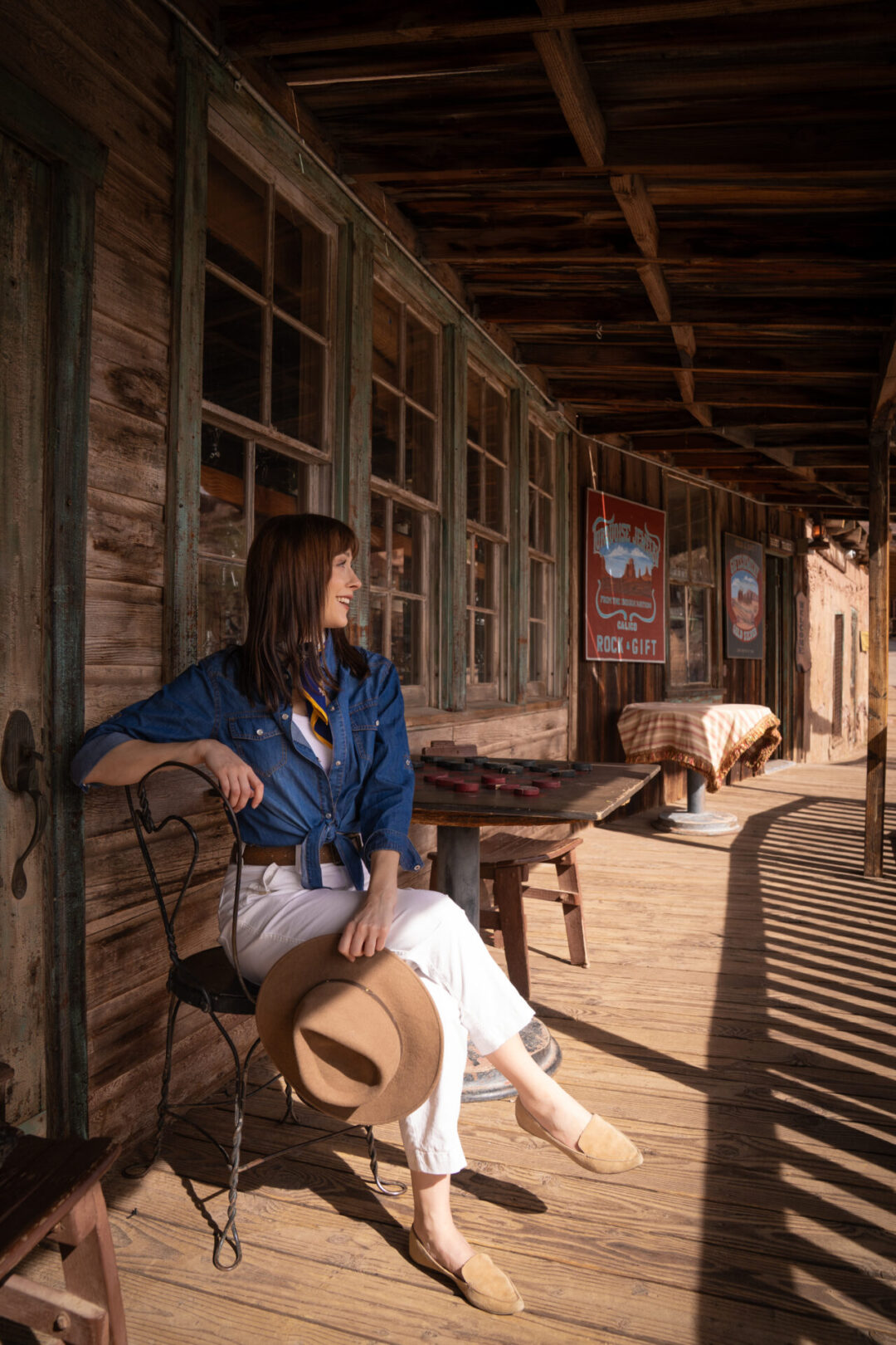 Travel Blogger Jordan Gassner sitting at a vintage wooden table with a chess set and looking out toward the main drag at Calico Ghost Town in California