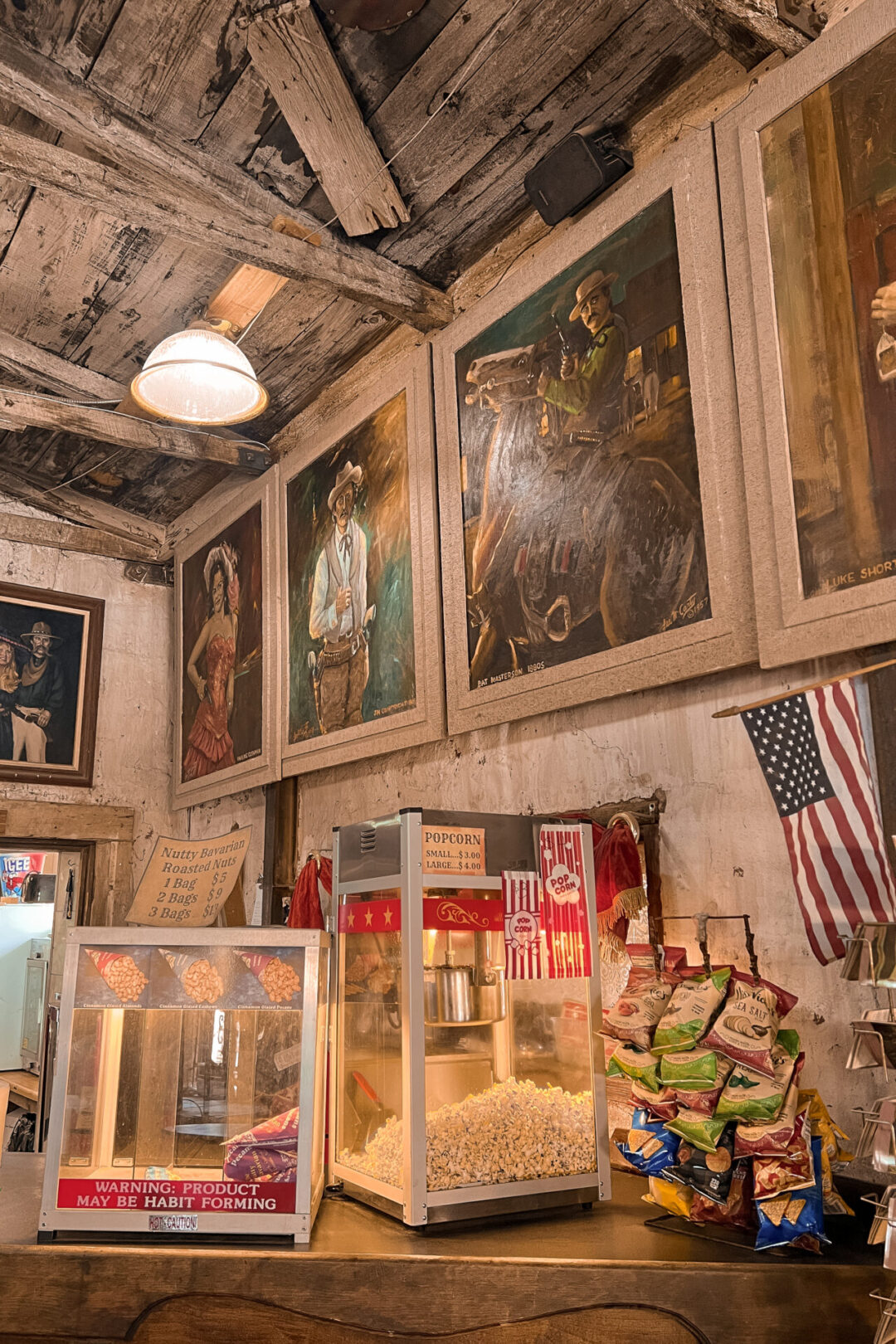 A popcorn machine sitting on a counter beneath some old west paintings inside the Saloon at Calico Ghost Town in California