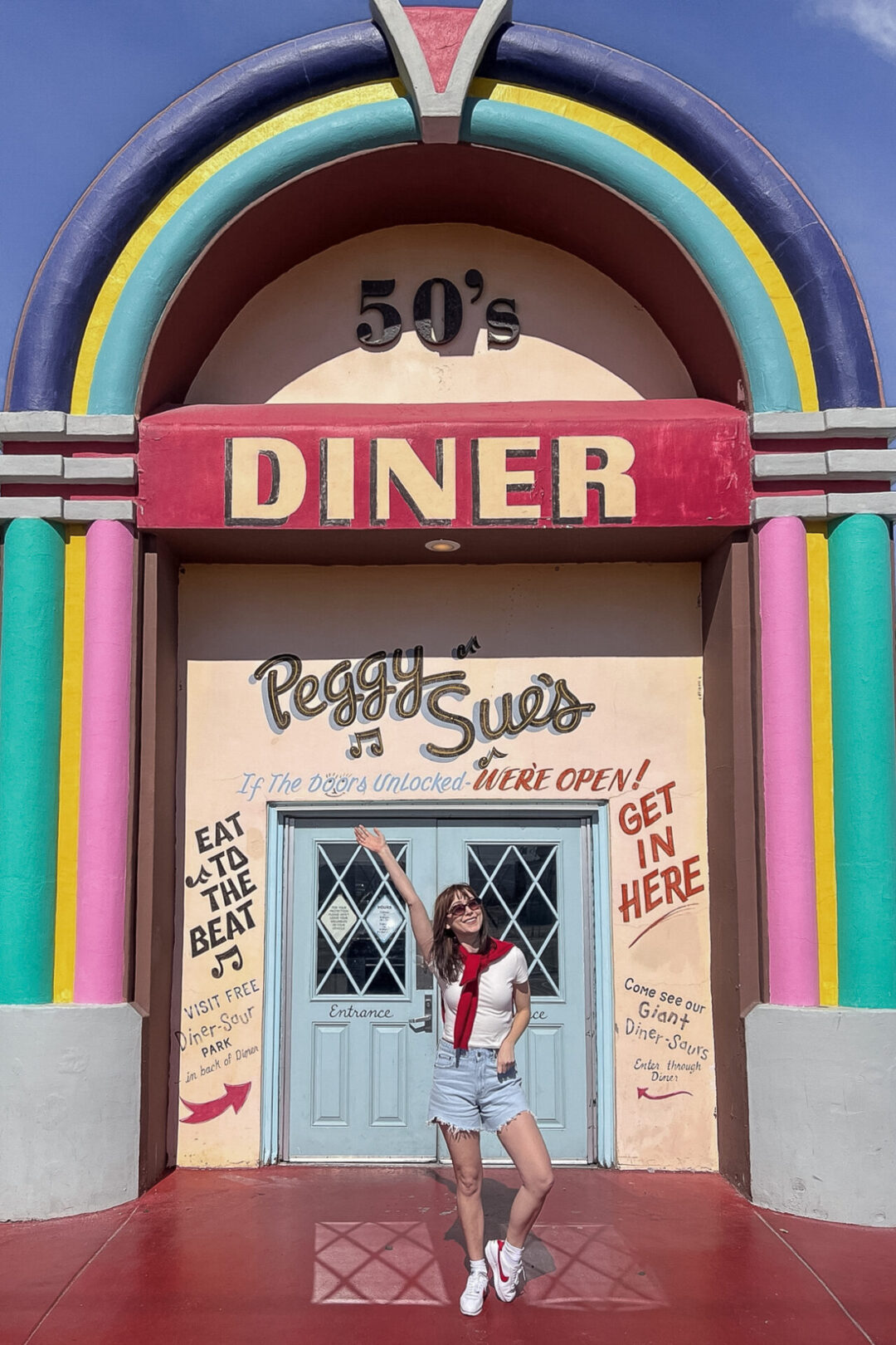 Travel Blogger Jordan Gassner holding her arm up and smiling in front of Peggy Sue's 50's Diner in California