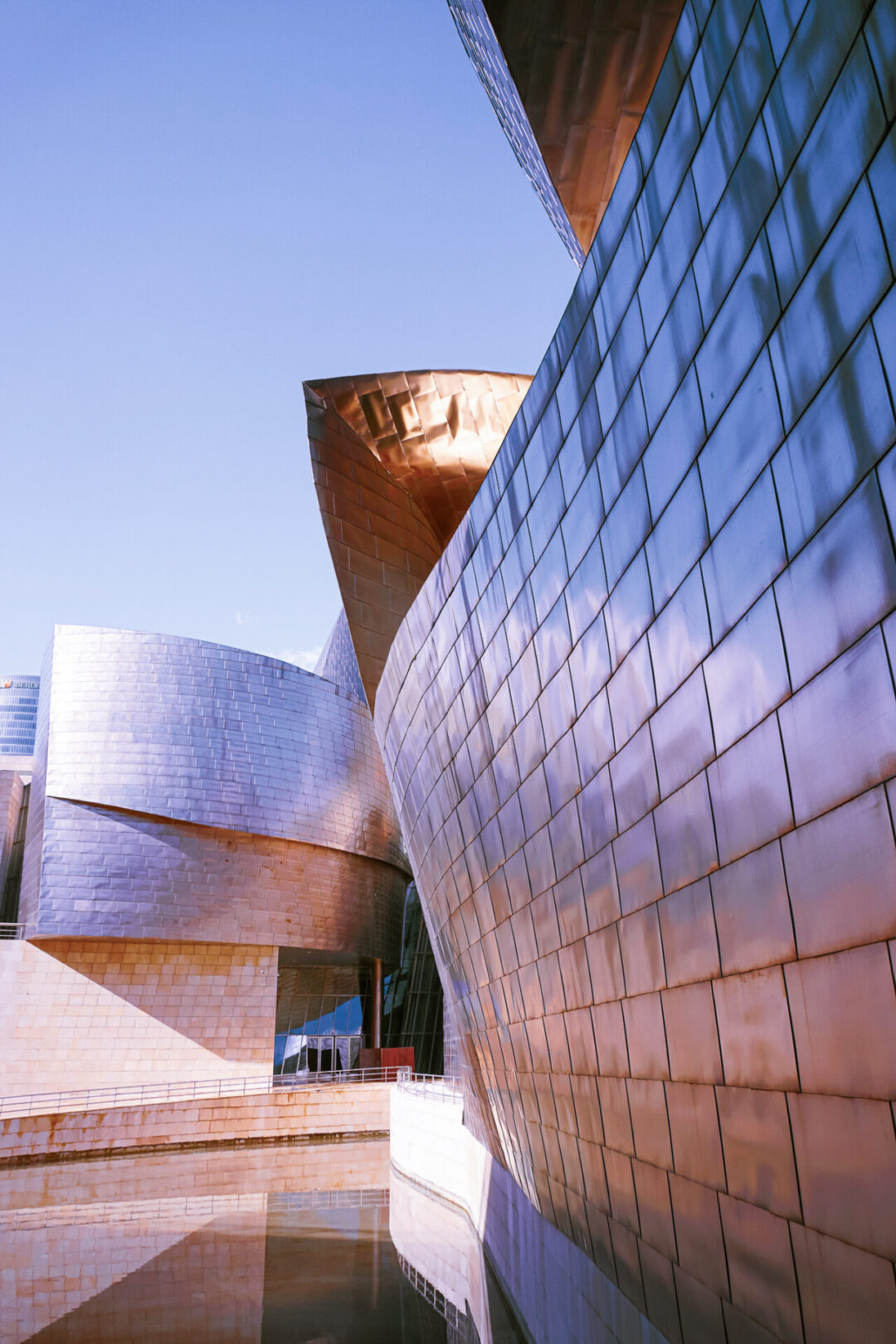 The silver Guggenheim building in Bilbao reflecting pink hues