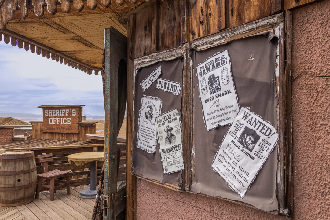 "Wanted" and "Reward!" posters hanging up on a bulletin board outside the Sheriff's Office at Calico Ghost Town in California