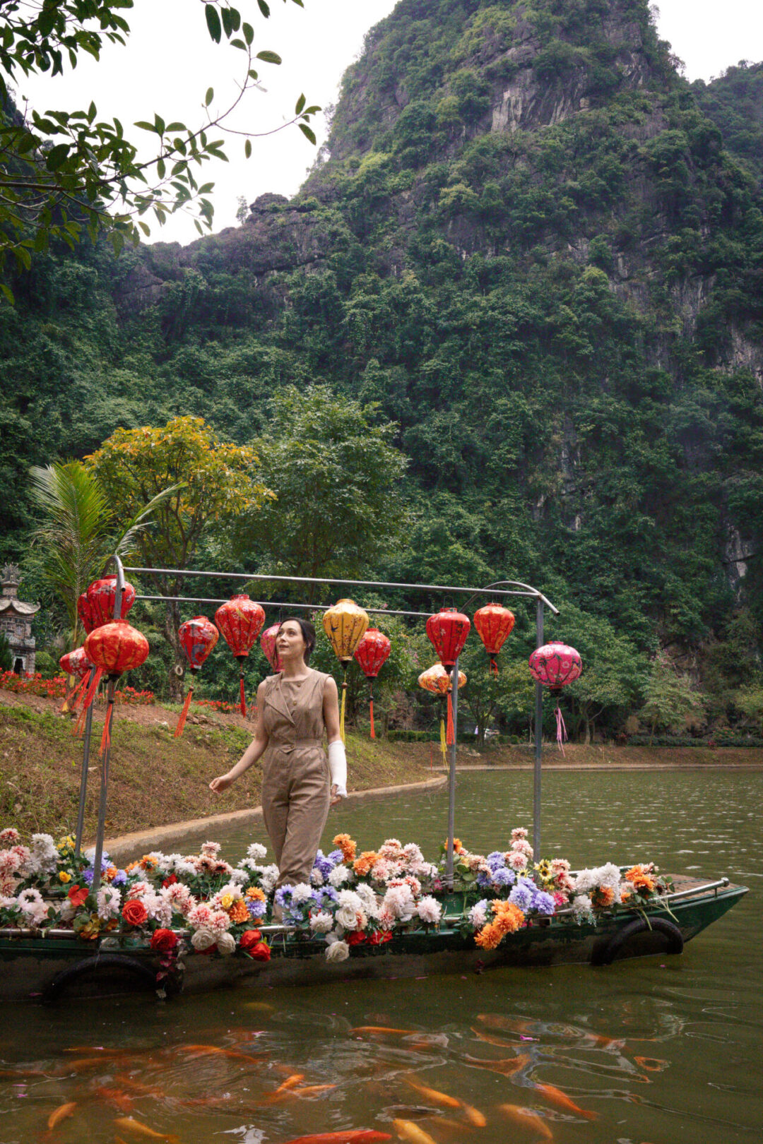 Things to do in Ninh Binh: Travel Blogger Jordan Gassner standing in a lantern and flower decorated boat on a lake inside Tuyet Tinh Coc in Ninh Binh, Vietnam