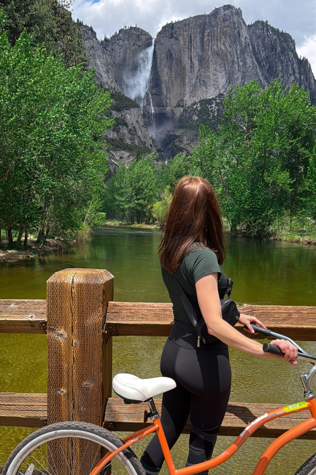 Travel Blogger Jordan Gassner walking an orange beach cruiser bike over a bridge near Yosemite Falls on a Yosemite weekend trip