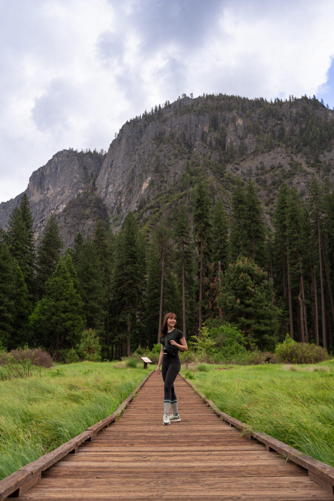 Travel Blogger Jordan Gassner looking out at the scenery from a wood boardwalk at Cook's Meadow Loop Trail in Yosemite, California