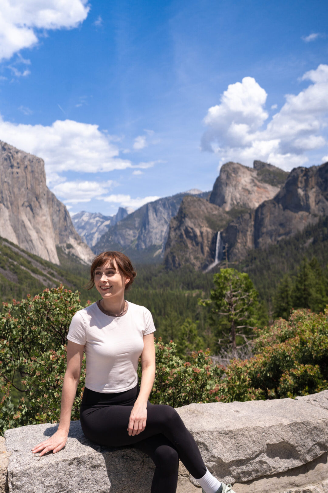 Travel Blogger Jordan Gassner smiling from the famous Tunnel View in Yosemite National Park, California. Half Dome, El Capitan, and Bridalveil Falls behind her