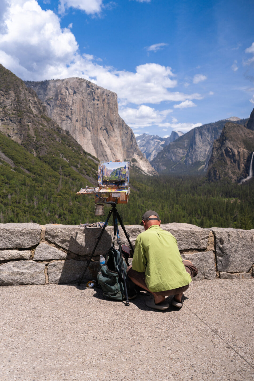 A painter digging through his bag of supplies in front of the Tunnel View lookout point with Half Dome, El Capitan, and Bridalveil Falls in Yosemite National Park in California