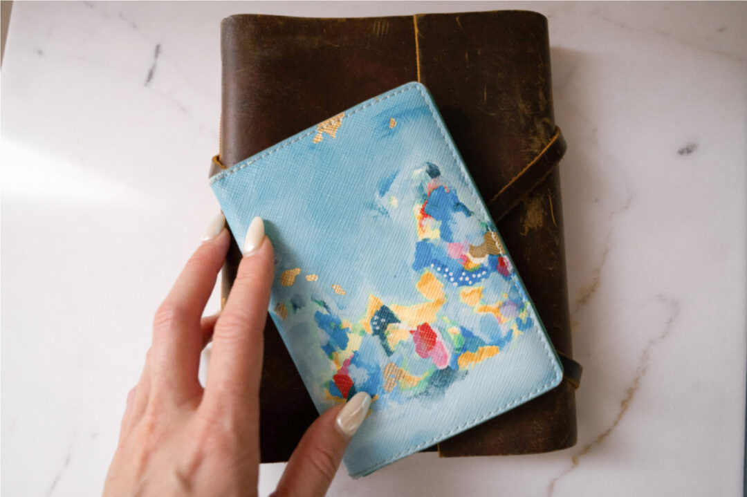 A woman's hand holding a passport cover and a journal