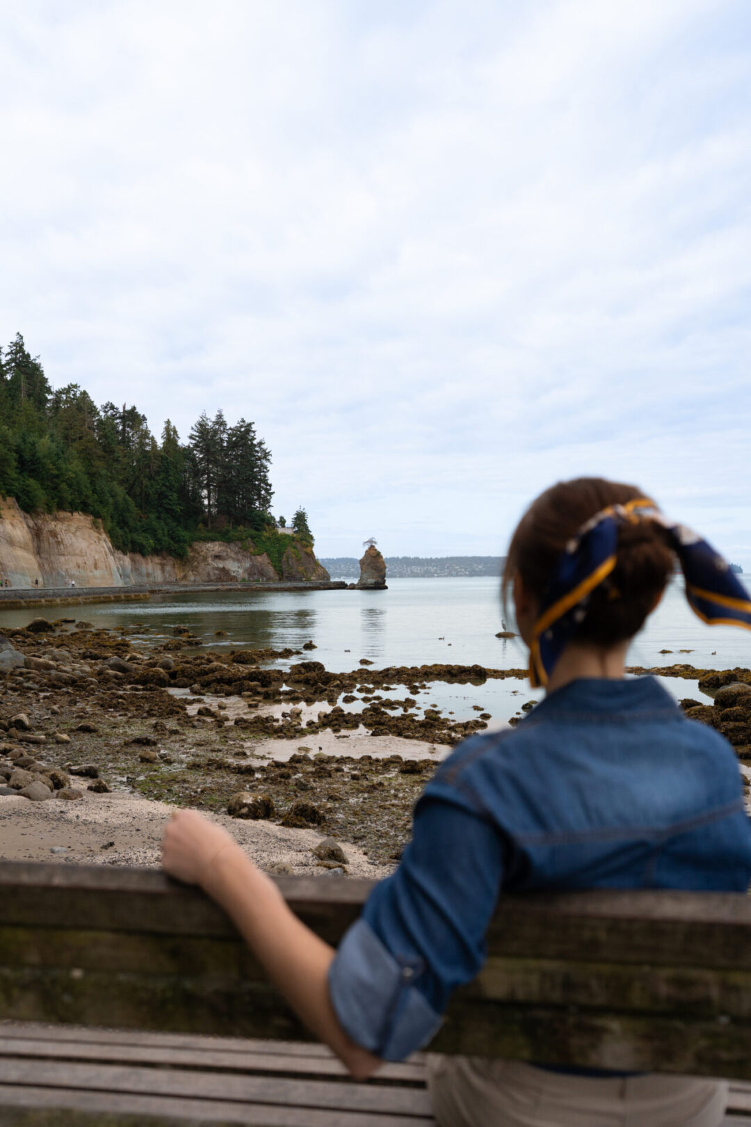 Travel Blogger Jordan Gassner sitting on a bench looking out at Siwash Rock in Stanley Park located in Vancouver's West End