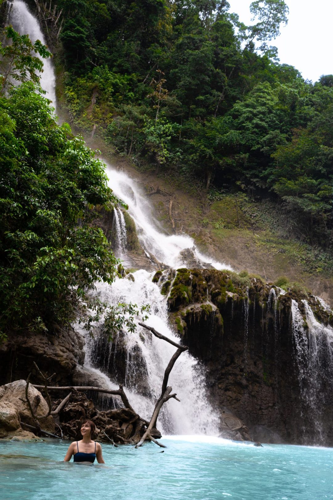 Travel Blogger Jordan Gassner sitting on a rock and looking up at the landscape from the turquoise pool at the base of Lapopu Waterfall on the remote Sumba island in Indonesia