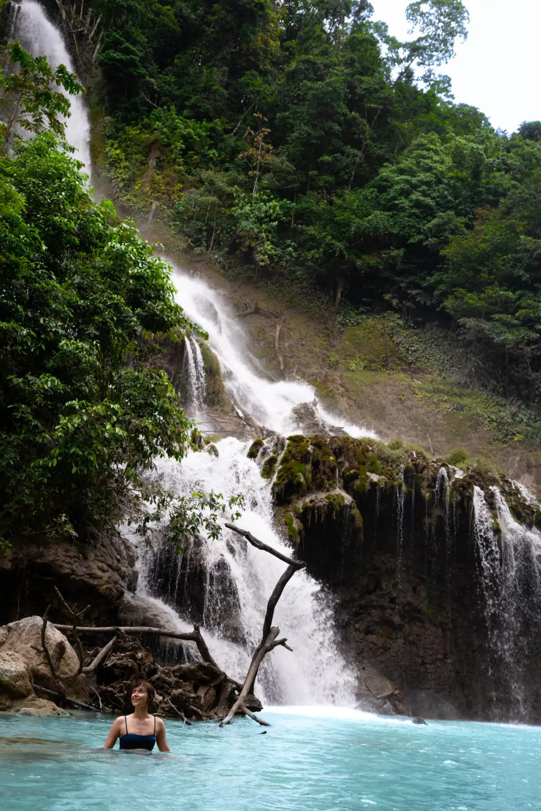 Travel Blogger Jordan Gassner sitting on a rock in the turquoise water at the base of Lapopu Waterfall in Sumba, Indonesia
