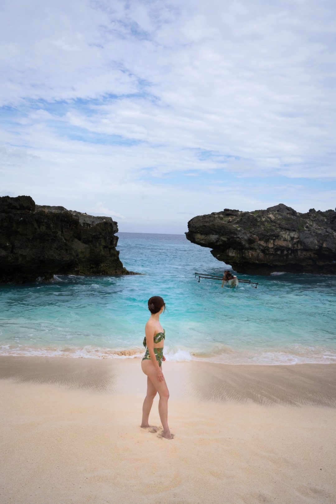 Travel Blogger Jordan Gassner walking along the sand at Mandorak Beach while a traditional boat pulls ashore on the island of Sumba, Indonesia