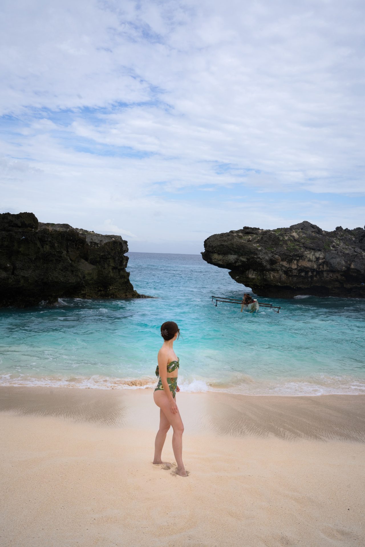 Travel Blogger Jordan Gassner walking along the sand of Mandorak Beach while a local fishing boat comes in with the high tide in Sumba, Indonesia