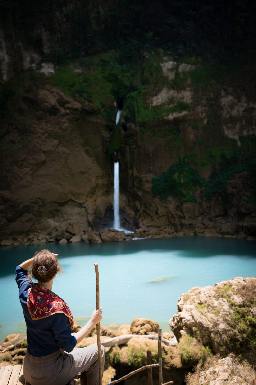 Travel Blogger Jordan Gassner sitting with a walking stick in hand and looking toward Matayangu Waterfall in Sumba, Indonesia