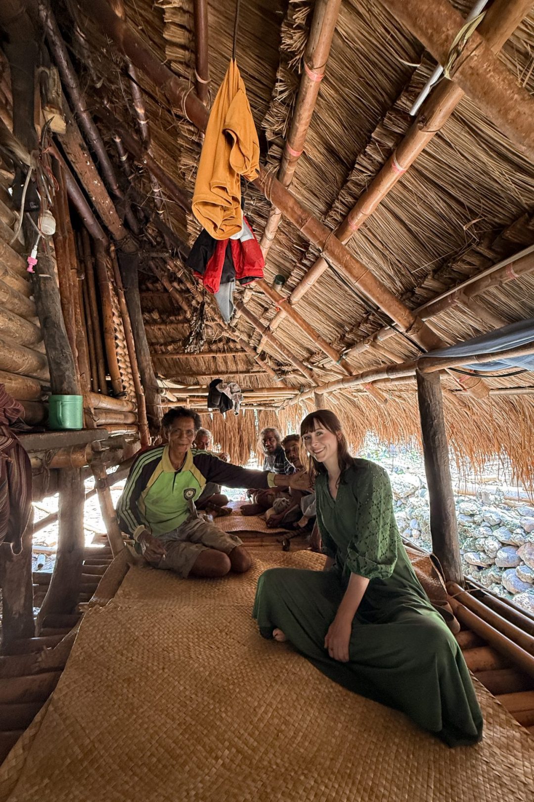 Travel Blogger Jordan Gassner smiling with a group of locals underneath the shade of a traditional home in the village of Yaru Wora, Sumba, Indonesia