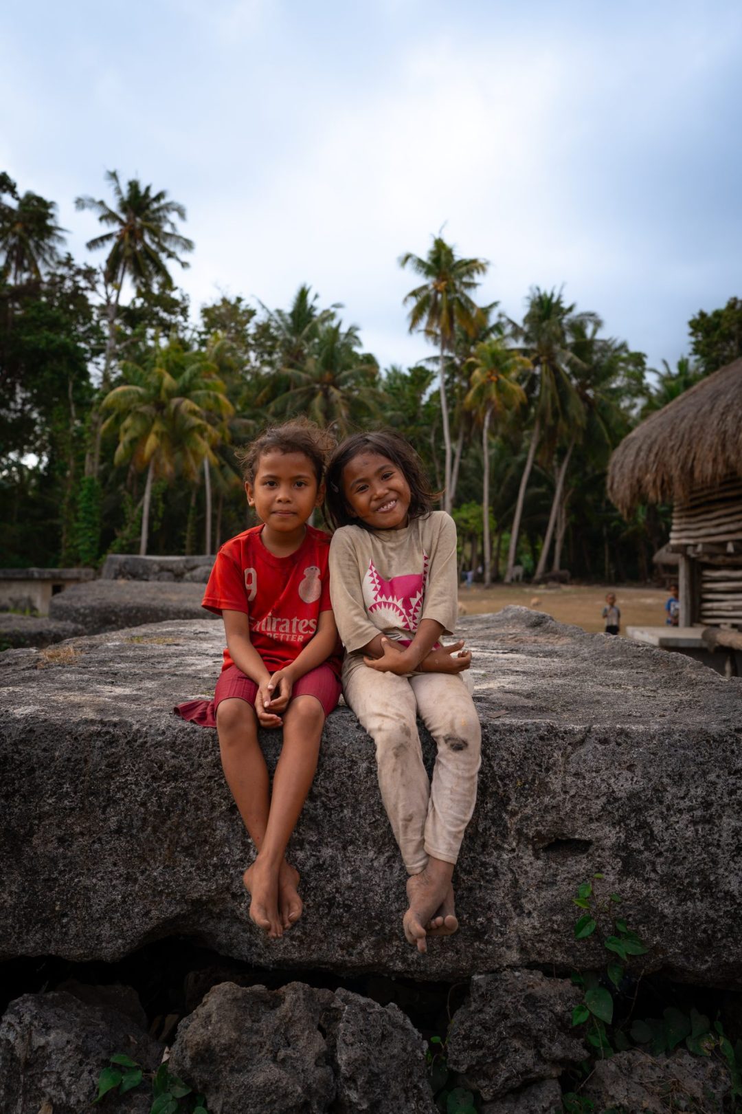 Two girls smiling while sitting on top of a megalithic tomb in the traditional village of Waikaroko in Sumba, Indonesia