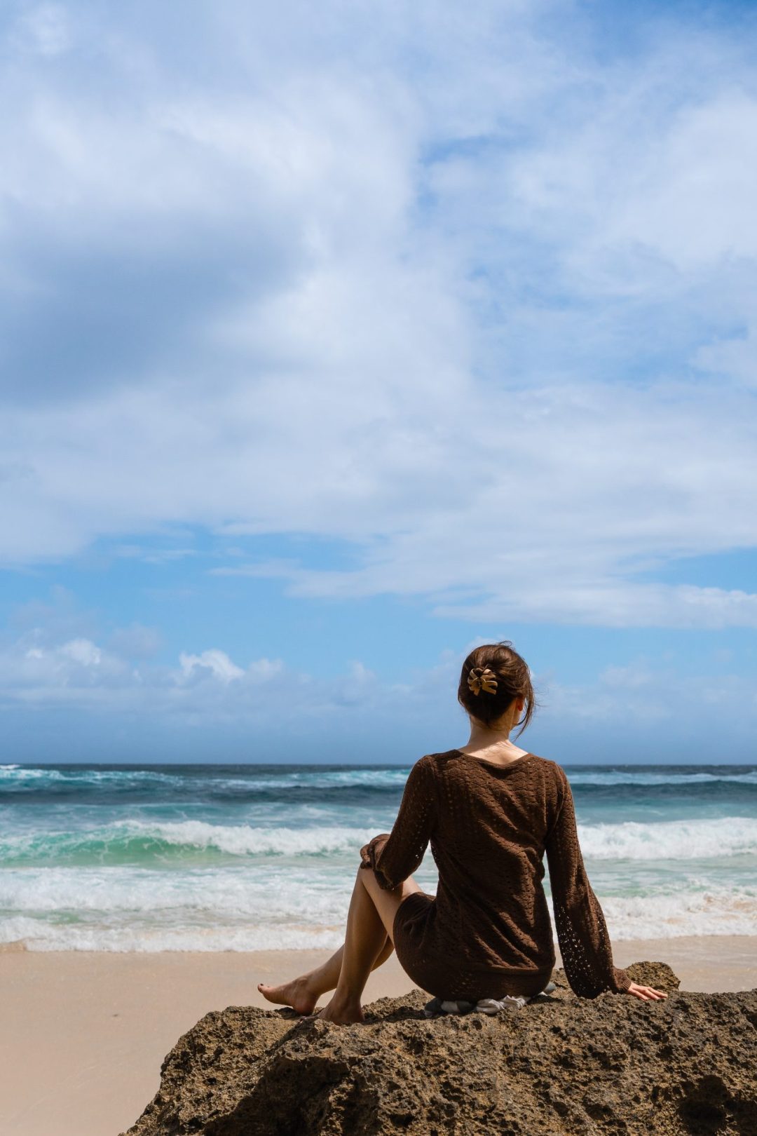 Travel Blogger Jordan Gassner sitting on a rock looking out over the turquoise water surrounding Sumba, Indonesia