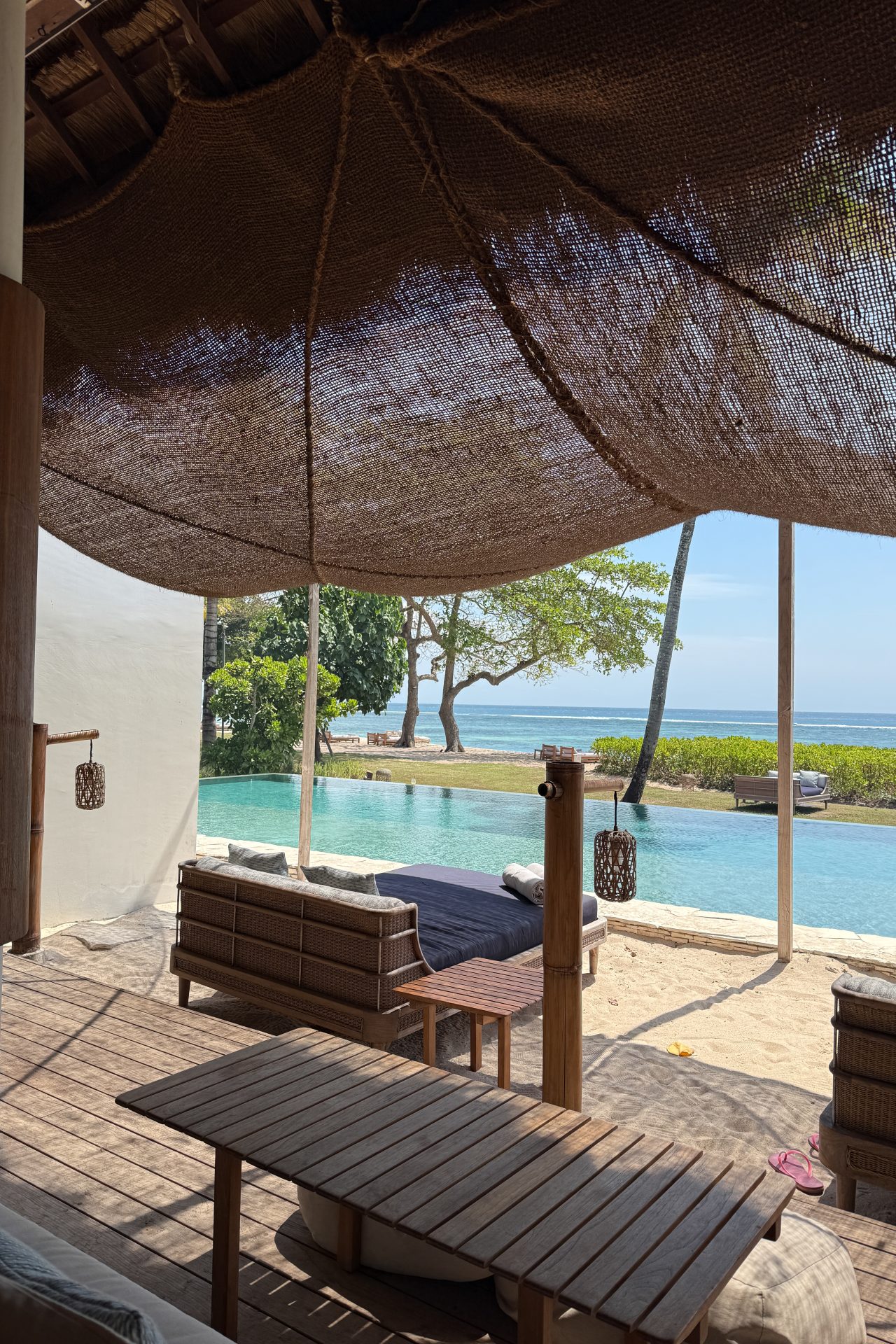 A few daybeds covered by a canvas awning in front of an infinity pool near the ocean at Cap Karoso Resort in Sumba, Indonesia