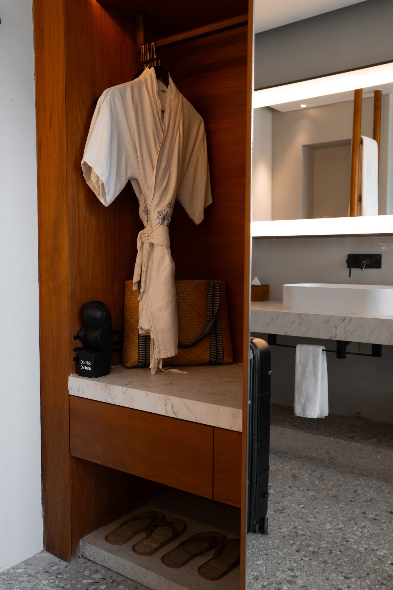 A closet with a robe, beach bag, sandals, and a "Do Not Disturb" carved owl inside a closet in one of the guest rooms at Cap Karoso resort in Sumba, Indonesia