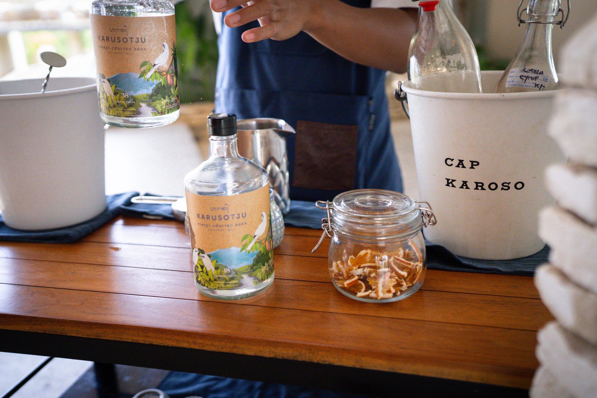 The bar cart filled with a jar of orange peels, a bucket of juices, a bucket of ice, and Karusotju alcohol at Cap Karoso Resort in Sumba, Indonesia