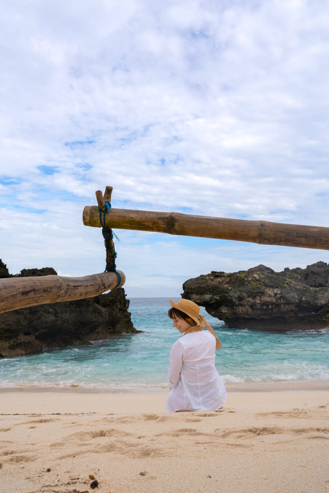 Travel Blogger Jordan Gassner sitting on Mandorak Beach wearing a sunhat in Sumba, Indonesia