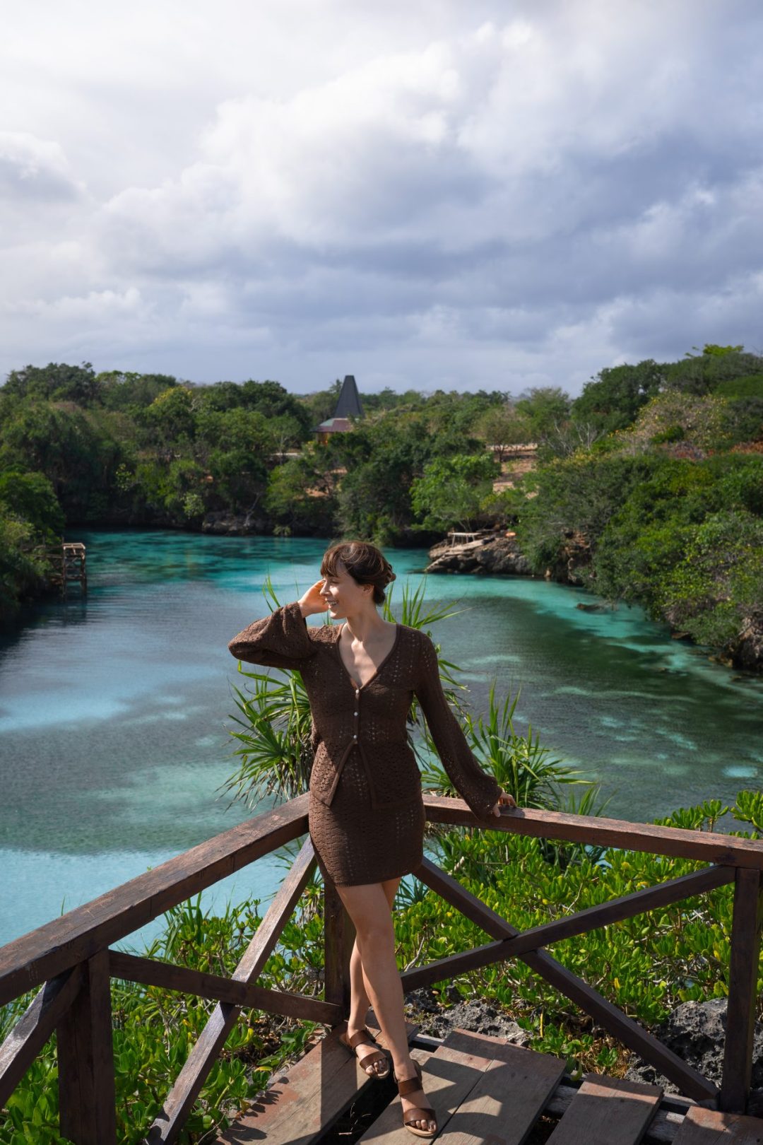 Travel Blogger Jordan Gassner looking over her shoulder while standing on a platform overlooking Waikuri Lagoon in Sumba, Indonesia