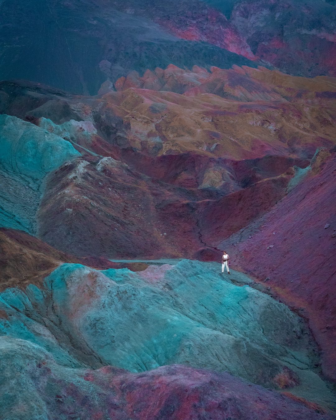 Travel Blogger Jordan Gassner walking along a path in between the colorful hills of Artist's Palette in Death Valley, California